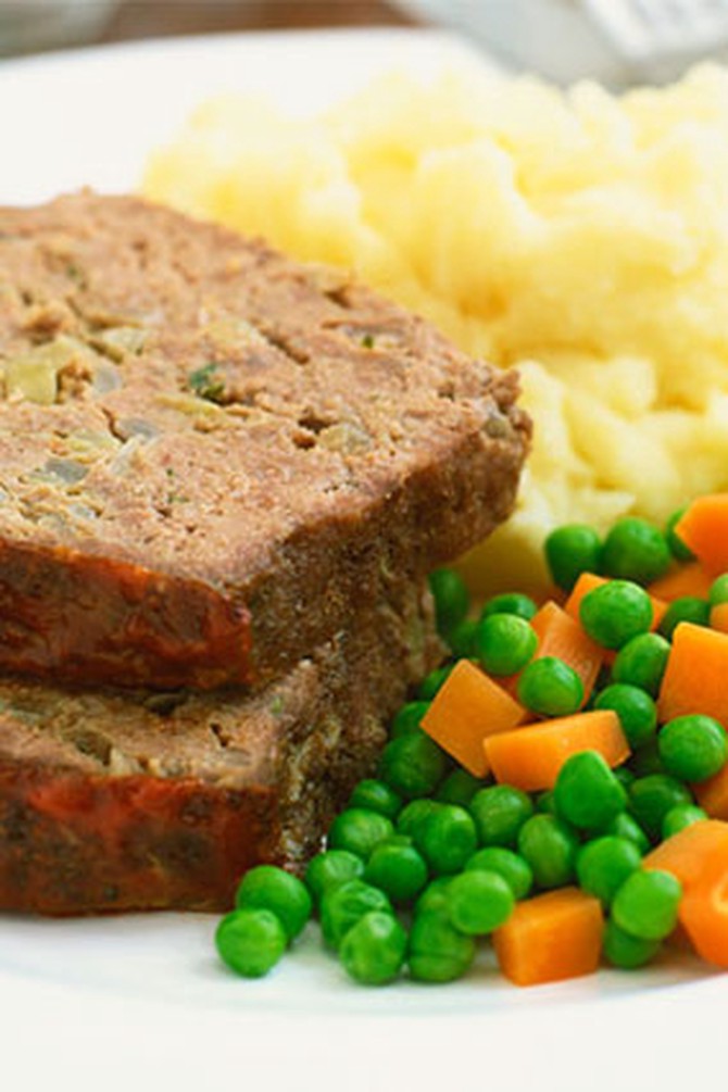 Slices of meatloaf on plate with peas and carrots and mashed potatoes