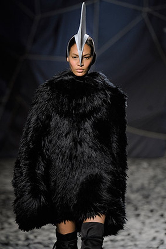 Runway model wearing large black fur and dorsal fin on head