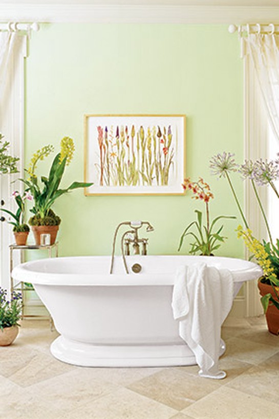 Pale green bathroom with freestanding bathtub, surrounded by potted plants