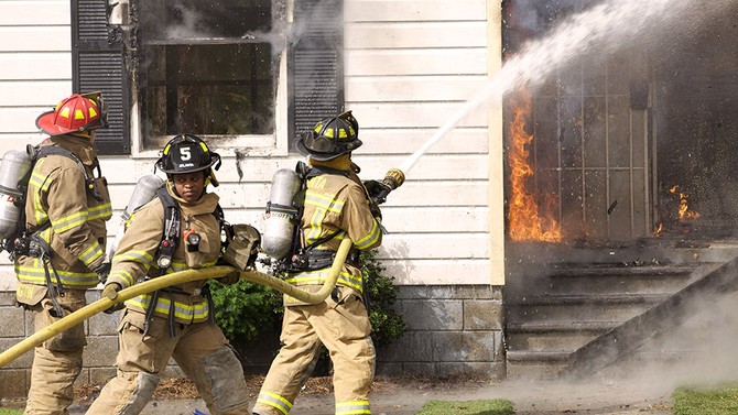 Firefighters aiming fire hose at burning house