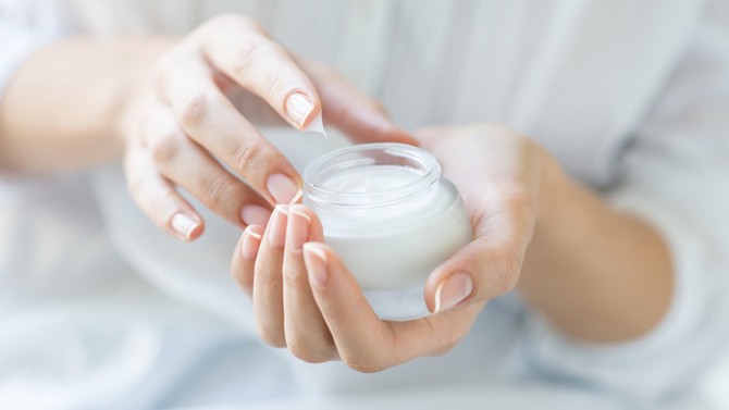 Woman dipping finger in lotion jar