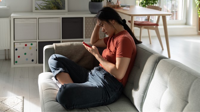 woman alone at home looking at her cell phone on the sofa