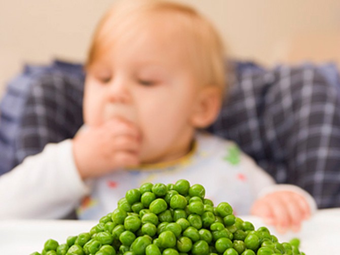 Child sitting behind a plate of peas