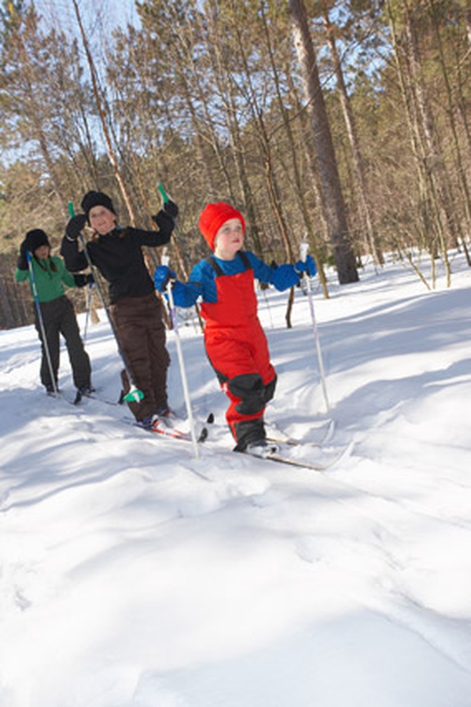 Young children cross-country skiing through the woods
