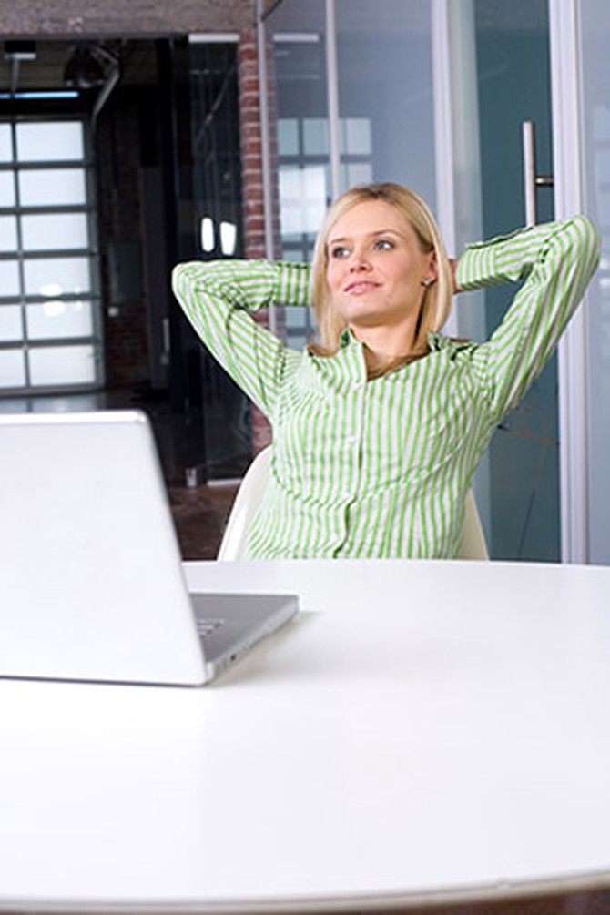 Woman seated in front of laptop with arms folded behind head