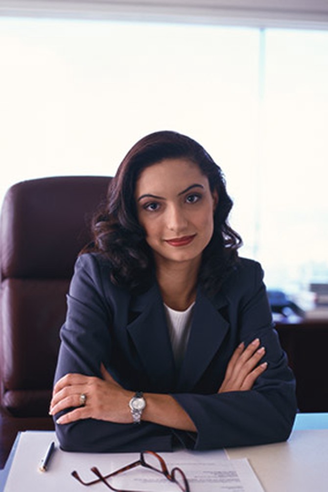 Woman executive sitting behind desk, arms folded